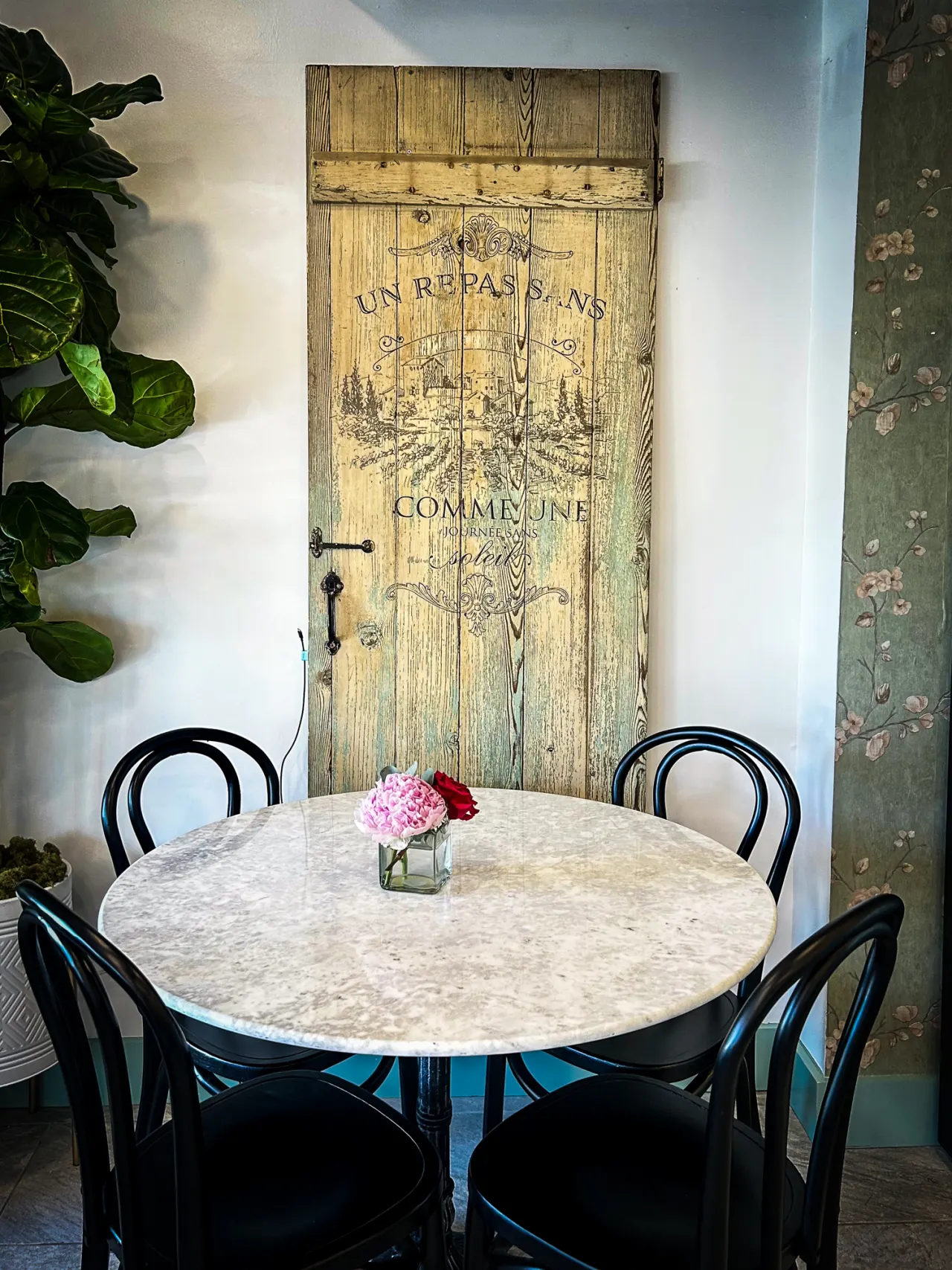 Restored vintage wood door inside Lincoln Perk Coffee, beside a fiddle leaf fig and marble café table