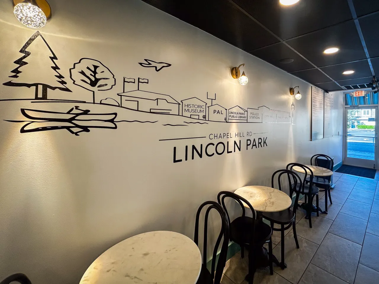 Hand-drawn Lincoln Park map mural with Chapel Hill Rd landmarks, marble bistro tables and bentwood chairs along the wall
